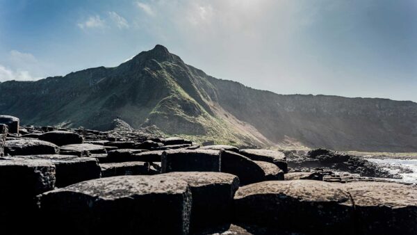 Giant's Causeway Private Driver Tour - A wide photo showing the stone formations at the Giant's Causeway in the foreground with a sharp tor rising behind them.